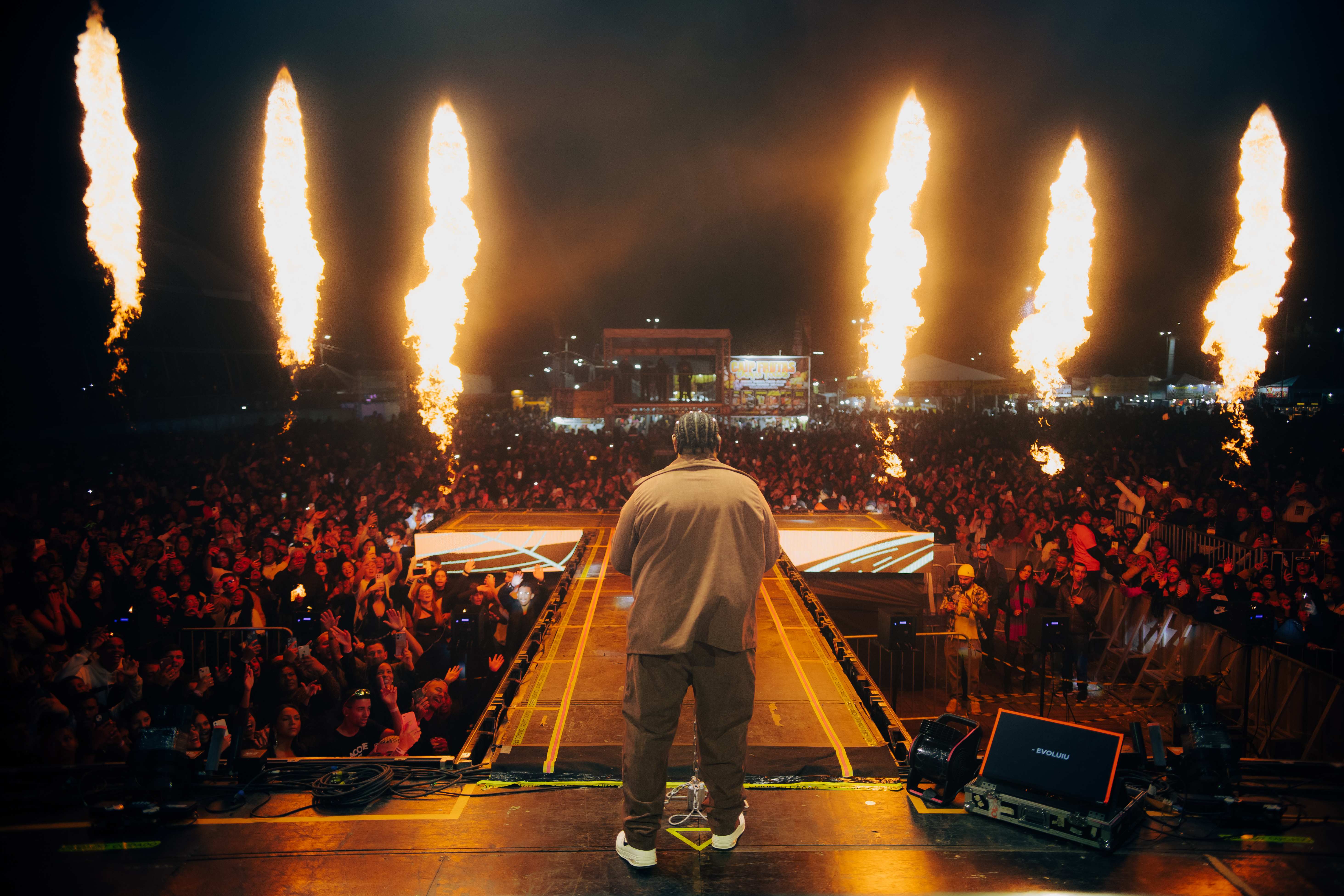 Kevin o Chris de costas no fim da passarela do palco diante de uma plateia lotada com colunas de fogo ao fundo